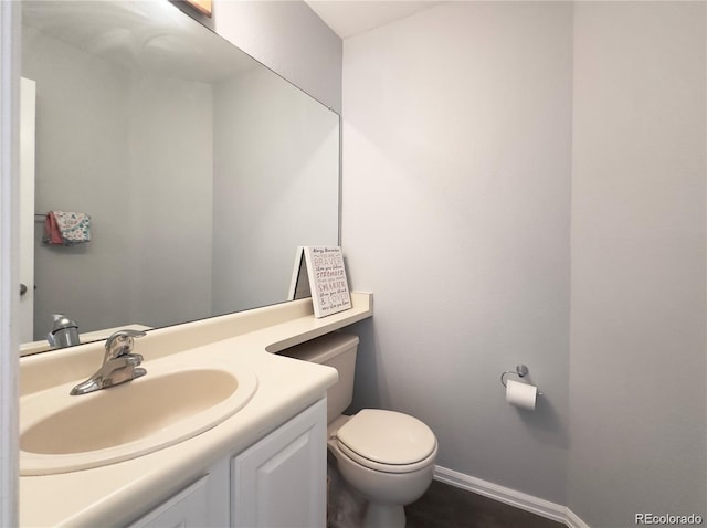 half bath with baseboards, vanity, and toilet