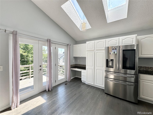 kitchen with vaulted ceiling with skylight, stainless steel fridge, white cabinetry, and dark wood-style flooring