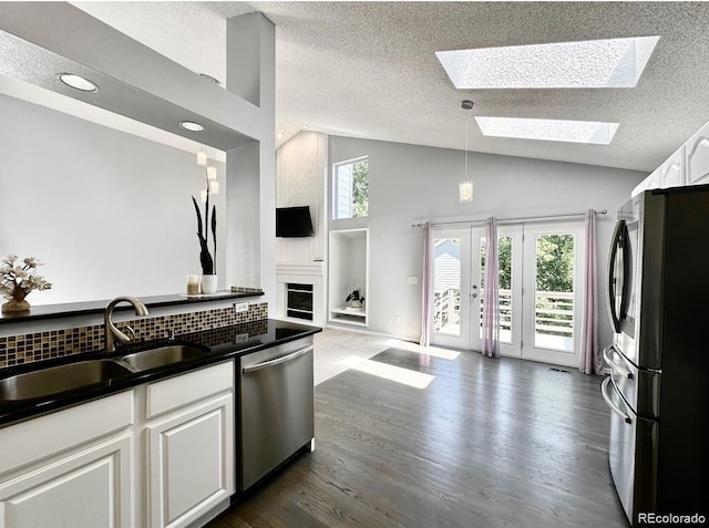 kitchen with stainless steel appliances, a skylight, white cabinetry, open floor plan, and dark countertops