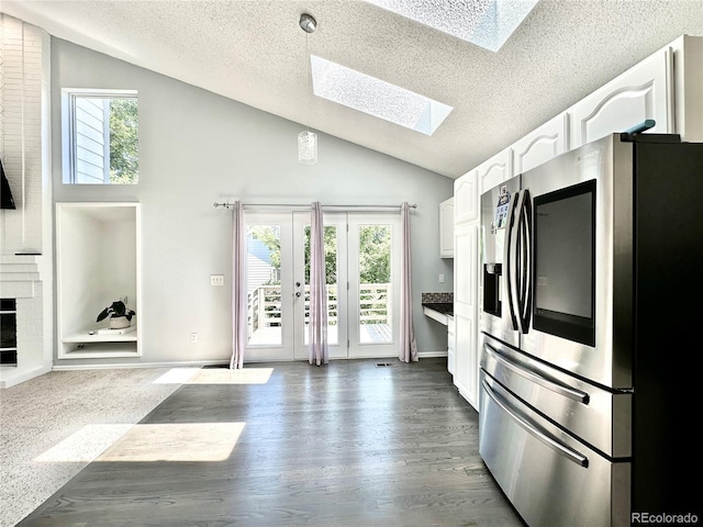 kitchen featuring dark wood-style floors, decorative light fixtures, white cabinetry, vaulted ceiling with skylight, and stainless steel fridge with ice dispenser