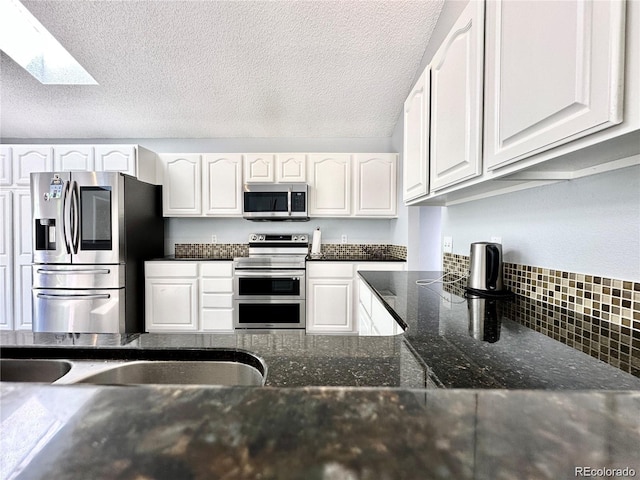 kitchen featuring a skylight, appliances with stainless steel finishes, white cabinets, and dark stone counters