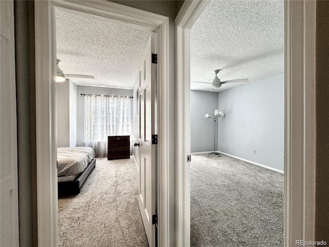 hallway featuring carpet floors, a textured ceiling, and baseboards