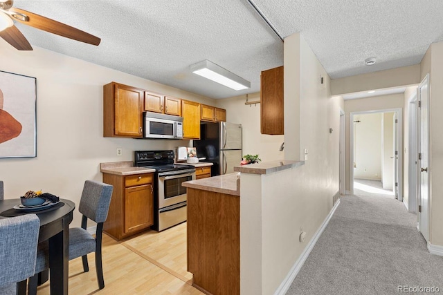 10212 W 80th Dr Unit C, Arvada, CO 80005 - kitchen featuring stainless steel appliances, brown cabinetry, a ceiling fan, light countertops, and a peninsula