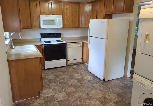 kitchen with white appliances, a sink, light countertops, stacked washer and dryer, and backsplash