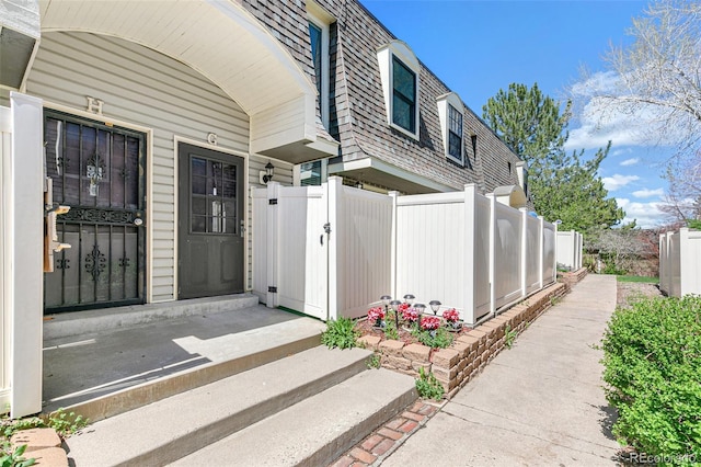 doorway to property with fence and mansard roof