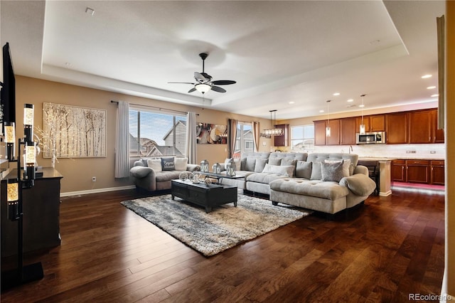 living room with dark hardwood / wood-style flooring, a raised ceiling, and a healthy amount of sunlight