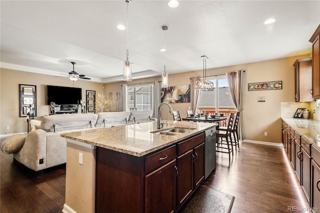 kitchen featuring an island with sink, decorative light fixtures, light stone countertops, and sink