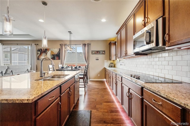 kitchen with an island with sink, sink, hanging light fixtures, stainless steel appliances, and dark wood-type flooring