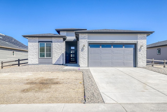 prairie-style home with concrete driveway, an attached garage, fence, and stone siding