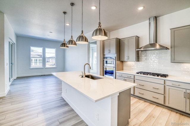 kitchen featuring light wood-type flooring, a sink, tasteful backsplash, appliances with stainless steel finishes, and wall chimney exhaust hood