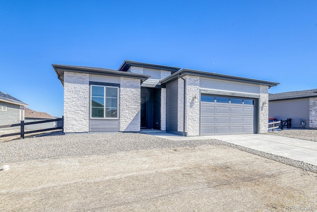 prairie-style house with concrete driveway, a garage, fence, and stone siding