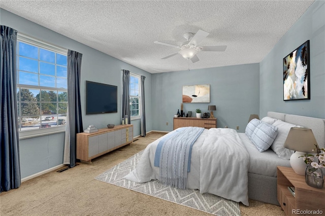 bedroom featuring a textured ceiling, light colored carpet, and ceiling fan