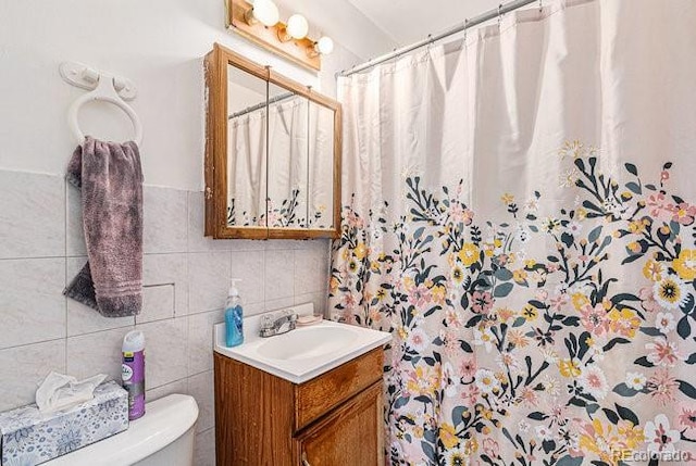 bathroom with vanity, toilet, tile walls, and walk in shower