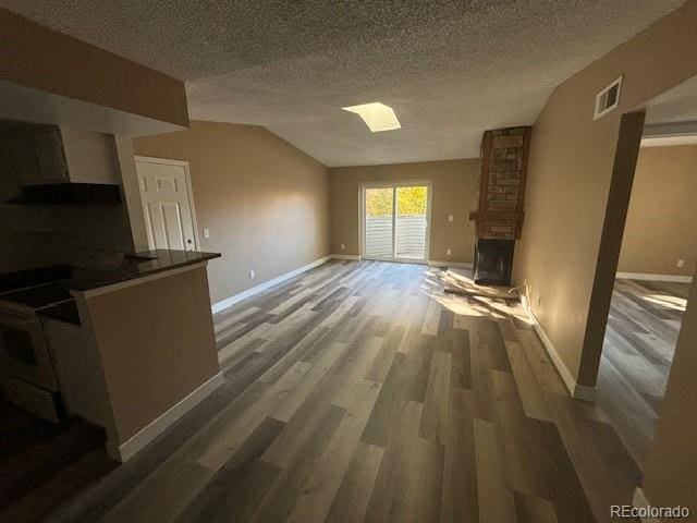 unfurnished living room with vaulted ceiling, a textured ceiling, a large fireplace, and dark hardwood / wood-style flooring