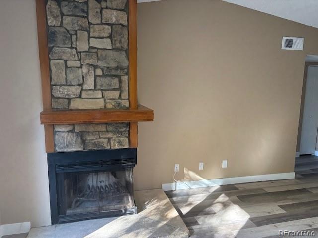 living room with a stone fireplace, hardwood / wood-style floors, and vaulted ceiling