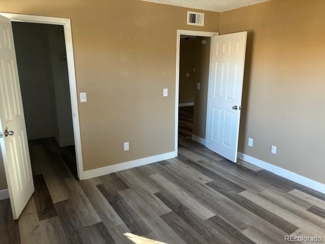 unfurnished bedroom featuring dark hardwood / wood-style floors, a textured ceiling, a closet, and a spacious closet