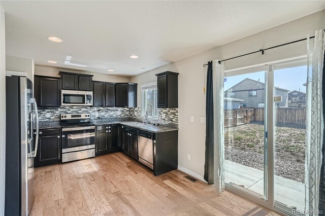 kitchen with light hardwood / wood-style flooring, tasteful backsplash, dark stone counters, stainless steel appliances, and sink