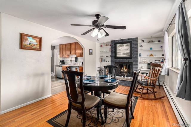 dining room featuring ceiling fan, a baseboard heating unit, a fireplace, light hardwood / wood-style floors, and built in shelves