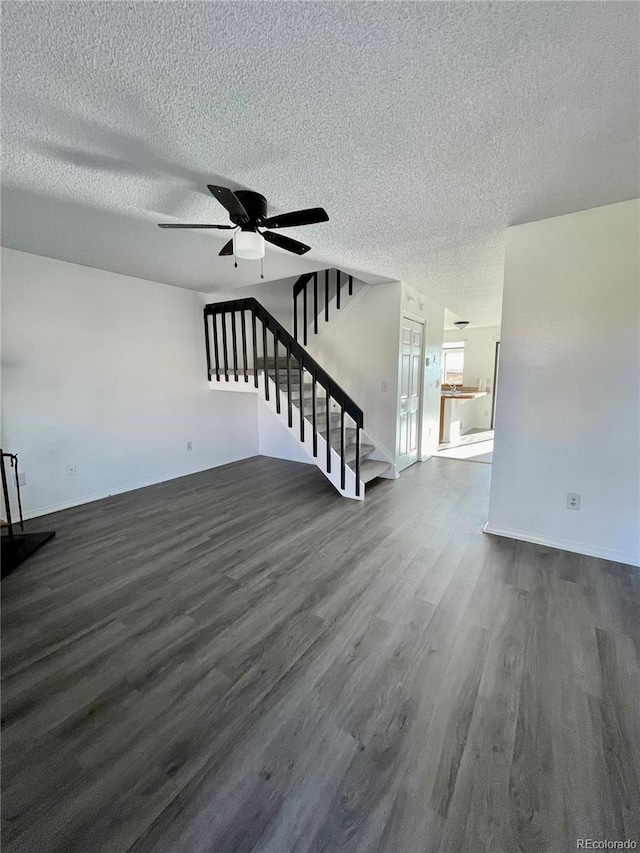 unfurnished living room featuring dark wood-type flooring, ceiling fan, and a textured ceiling