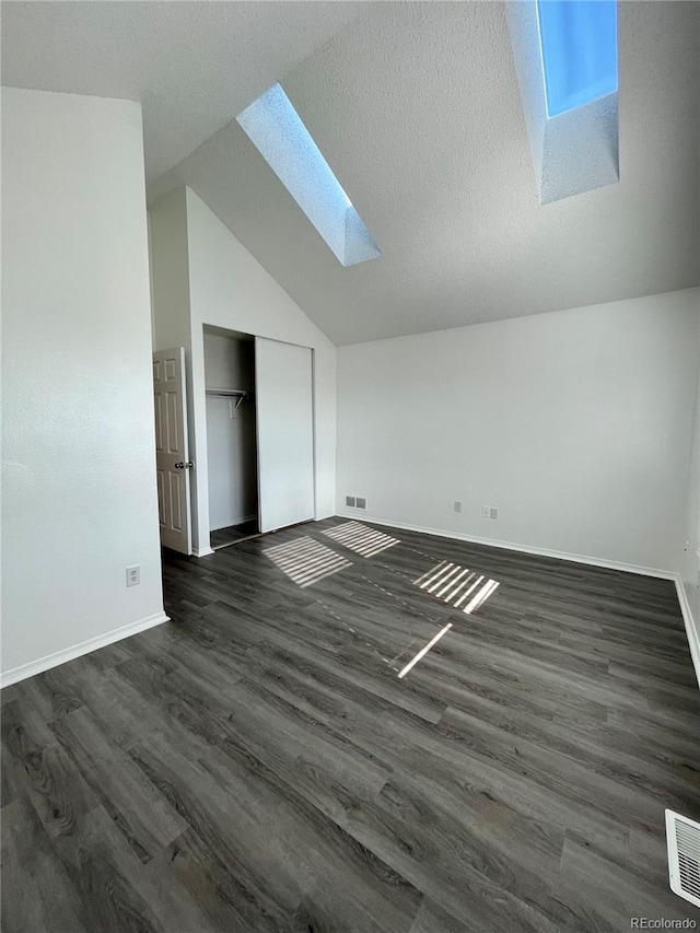 interior space featuring dark wood-type flooring, a closet, and vaulted ceiling with skylight