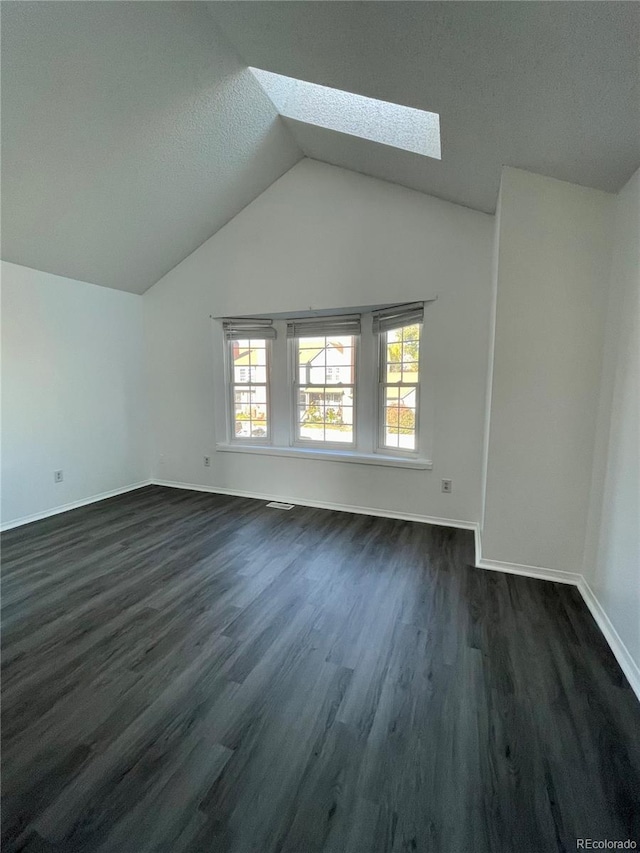 empty room featuring dark hardwood / wood-style floors, vaulted ceiling with skylight, and a textured ceiling