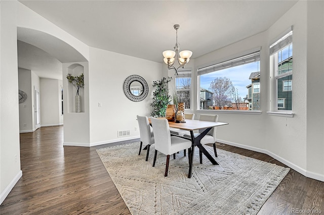 dining space featuring a chandelier, wood finished floors, baseboards, visible vents, and arched walkways