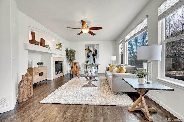 living area with baseboards, ceiling fan, dark wood-type flooring, and a tile fireplace