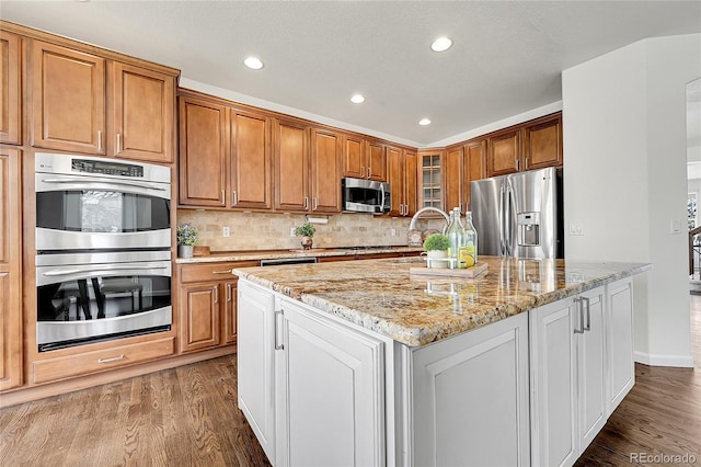 kitchen featuring dark wood-style floors, appliances with stainless steel finishes, light stone counters, and glass insert cabinets