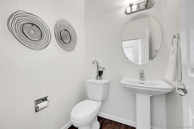 half bathroom with baseboards, wood finished floors, toilet, and a sink