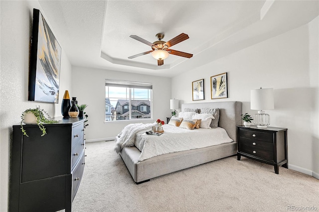 bedroom featuring a raised ceiling, baseboards, light colored carpet, and a textured ceiling