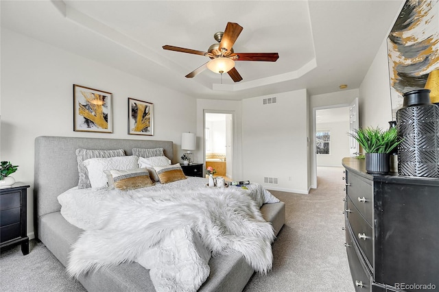 bedroom with a tray ceiling, light colored carpet, visible vents, and baseboards