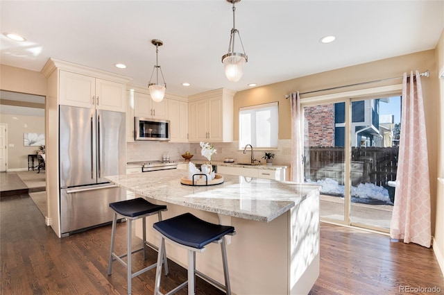 kitchen featuring dark hardwood / wood-style flooring, light stone counters, stainless steel appliances, decorative light fixtures, and a center island