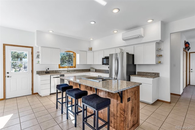 kitchen with appliances with stainless steel finishes, light stone counters, sink, white cabinets, and a kitchen island