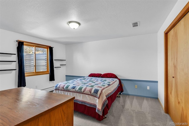 bedroom with light carpet, wooden walls, a textured ceiling, a baseboard radiator, and a closet