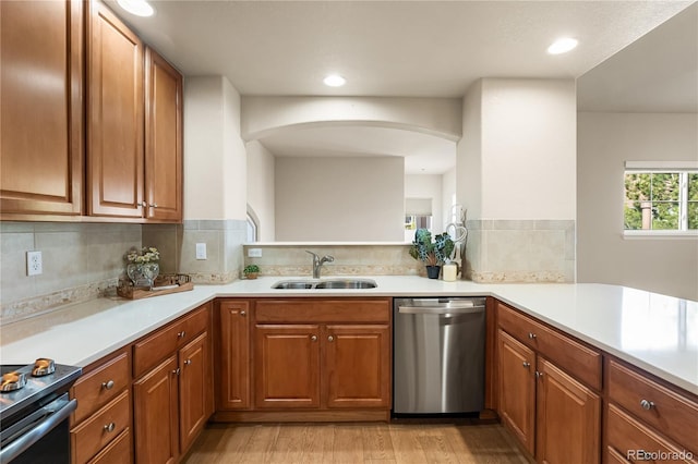 kitchen with appliances with stainless steel finishes, a sink, light wood-style flooring, brown cabinets, and decorative backsplash