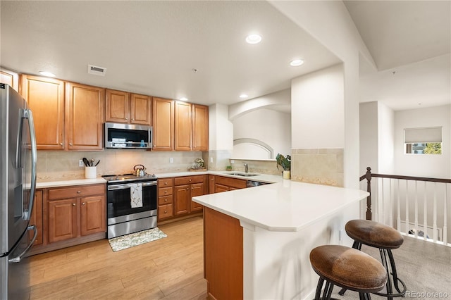 kitchen with stainless steel appliances, a peninsula, a sink, a kitchen bar, and light wood-style floors