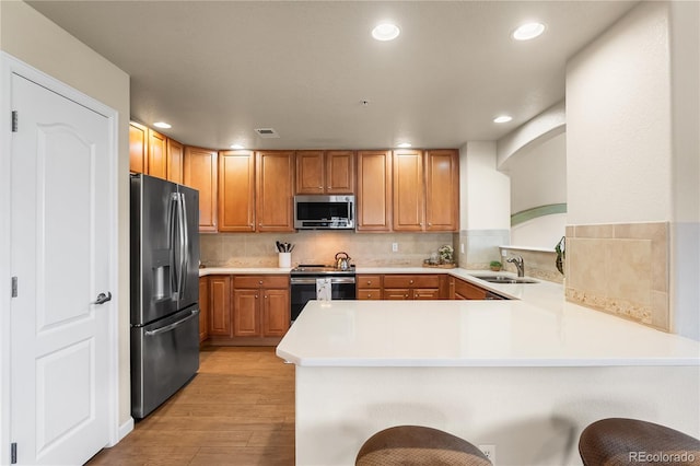 kitchen featuring stainless steel appliances, a peninsula, a sink, light wood-style flooring, and light countertops