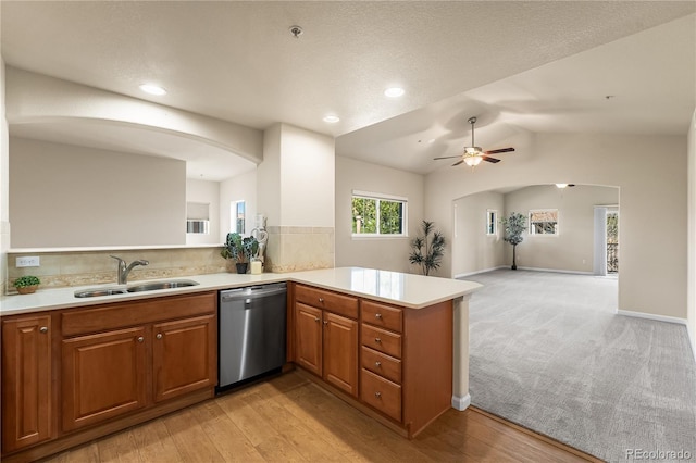kitchen with stainless steel dishwasher, a sink, a peninsula, brown cabinets, and light countertops