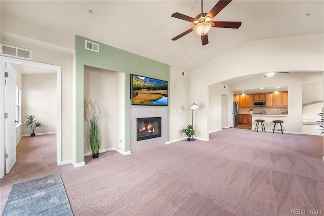unfurnished living room featuring light carpet, a ceiling fan, a tiled fireplace, baseboards, and high vaulted ceiling