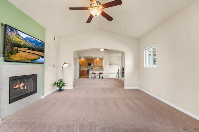 unfurnished living room featuring ceiling fan, light carpet, arched walkways, a fireplace, and vaulted ceiling