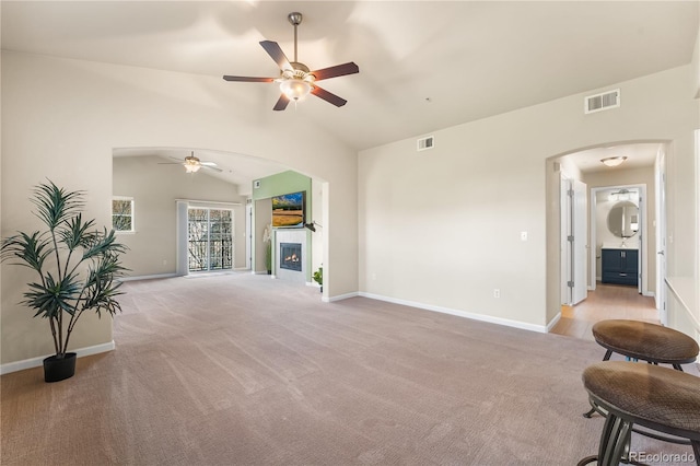 unfurnished living room featuring a ceiling fan, arched walkways, light colored carpet, vaulted ceiling, and baseboards