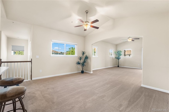 unfurnished room with a ceiling fan, vaulted ceiling, light carpet, arched walkways, and baseboards