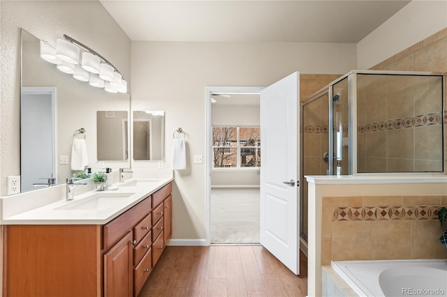 bathroom featuring wood finished floors, a shower stall, double vanity, and tiled bath