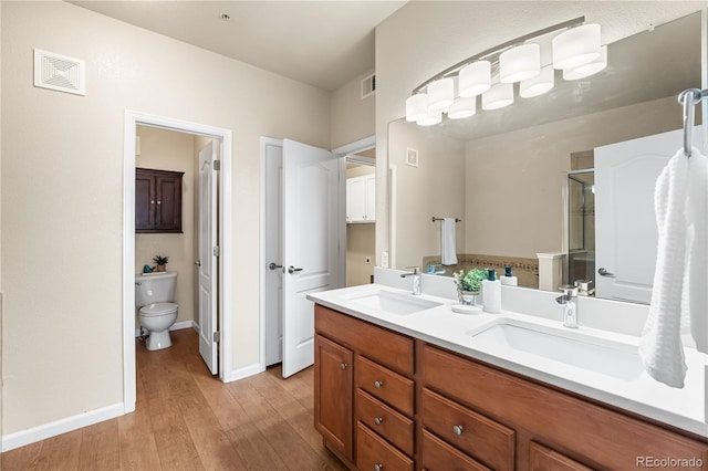 bathroom with toilet, wood finished floors, a shower stall, double vanity, and baseboards