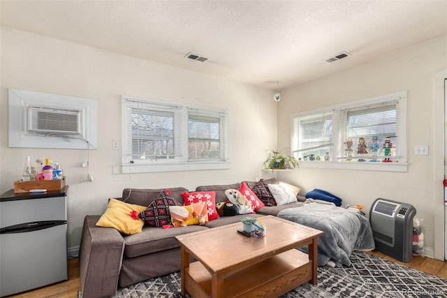 living room featuring hardwood / wood-style flooring, a textured ceiling, and a wall unit AC