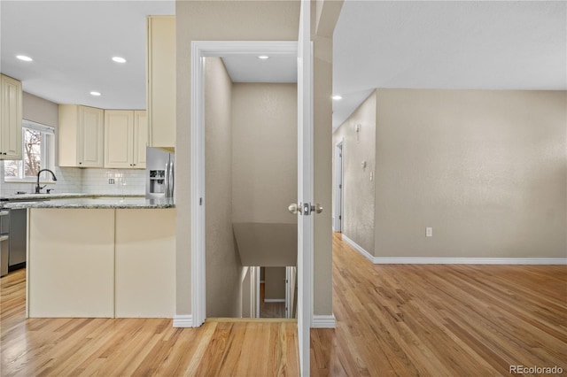 kitchen featuring decorative backsplash, stainless steel fridge, cream cabinets, and light wood-style floors