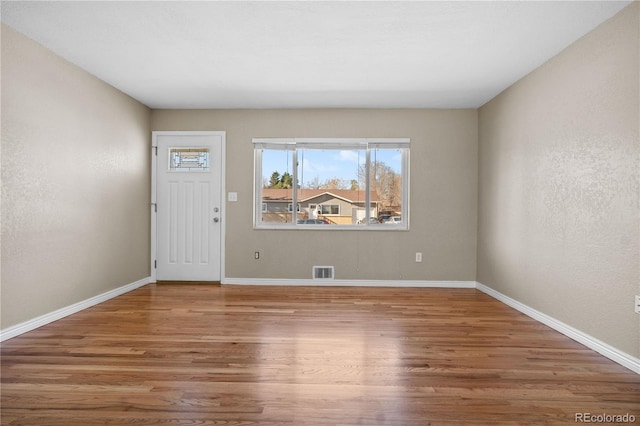 entrance foyer featuring a textured wall, visible vents, baseboards, and wood finished floors