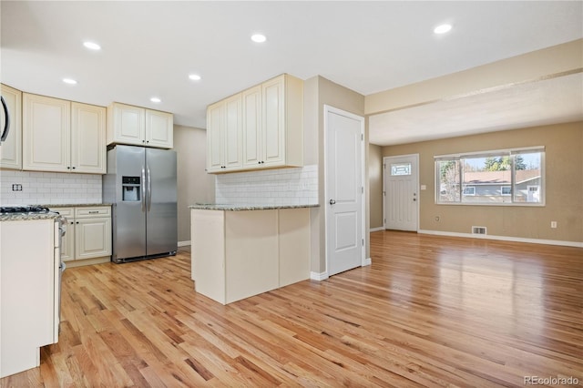 kitchen with visible vents, light stone counters, decorative backsplash, light wood-style floors, and stainless steel refrigerator with ice dispenser