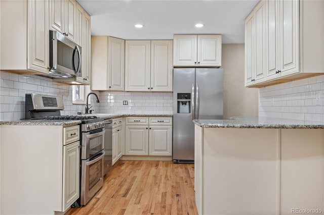 kitchen featuring a sink, tasteful backsplash, stainless steel appliances, light wood finished floors, and light stone countertops