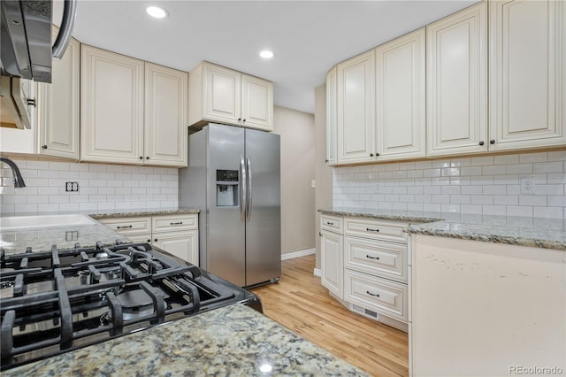 kitchen with light stone counters, stainless steel fridge with ice dispenser, a sink, cream cabinetry, and light wood-style floors